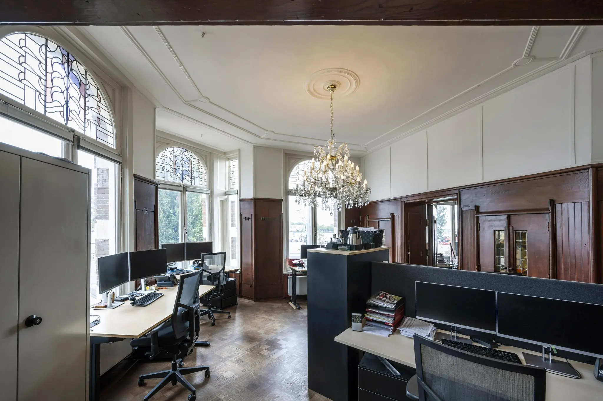 Klassiek ingerichte kantoorruimte aan de De Ruijterkade met houten lambrisering, hoge ramen met glas-in-lood en een grote kristallen kroonluchter.